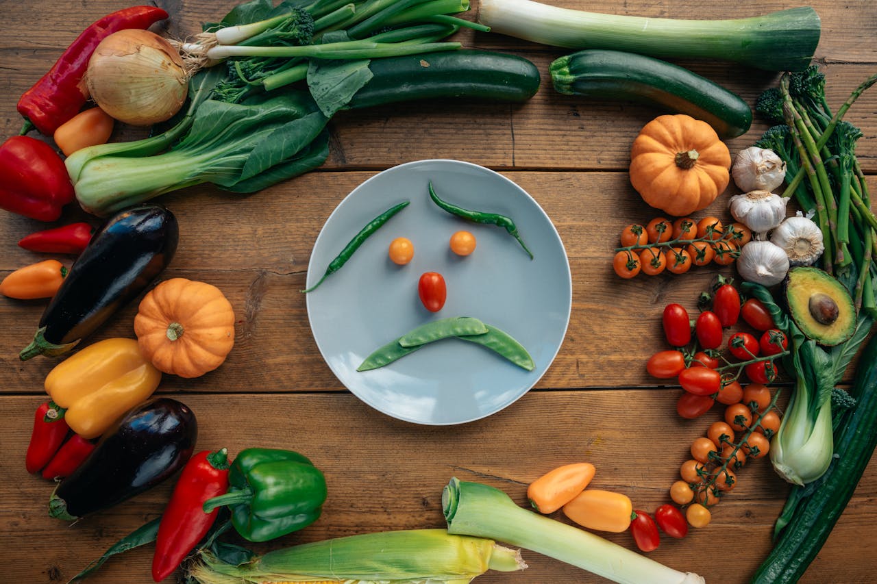 Playful vegetable arrangement creating a sad face on a plate surrounded by fresh produce.